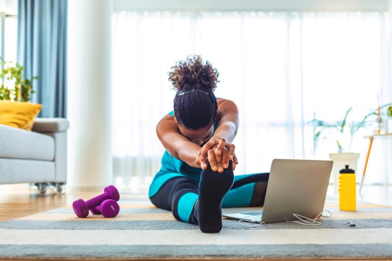a woman stretching on the floor in front of her laptop
